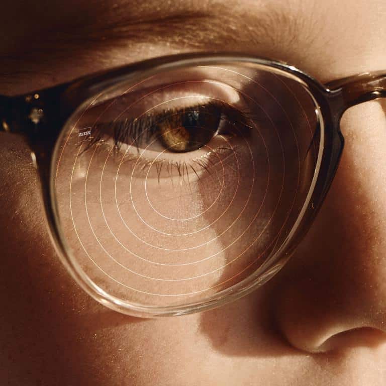 Close-up of a person wearing glasses, showing concentric circles reflected on the lens near their eye.