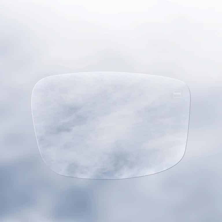 A transparent eyeglass lens floats in front of a cloudy sky, blending into the background except for its faint outline.